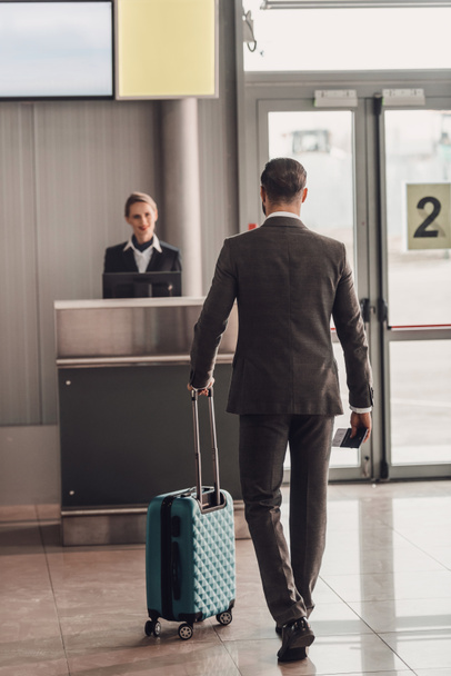 vista trasera del hombre de negocios caminando al mostrador de facturación del aeropuerto
 - Foto, Imagen