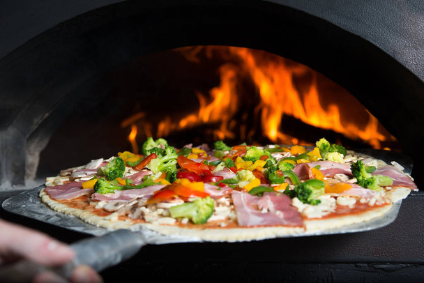 Man makes homemade pizza and he is inserted it to the hot slove which is burning by wood. - Photo, Image