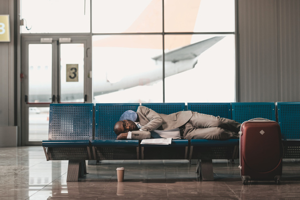 Erschöpfter Geschäftsmann schläft auf Sitzen, während er in der Flughafenlobby auf seinen Flug wartet - Foto, Bild