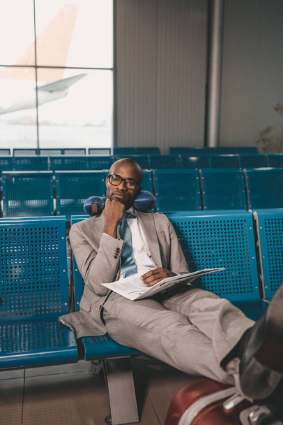 aburrido hombre de negocios con almohada de viaje esperando el vuelo en el vestíbulo del aeropuerto
 - Foto, Imagen