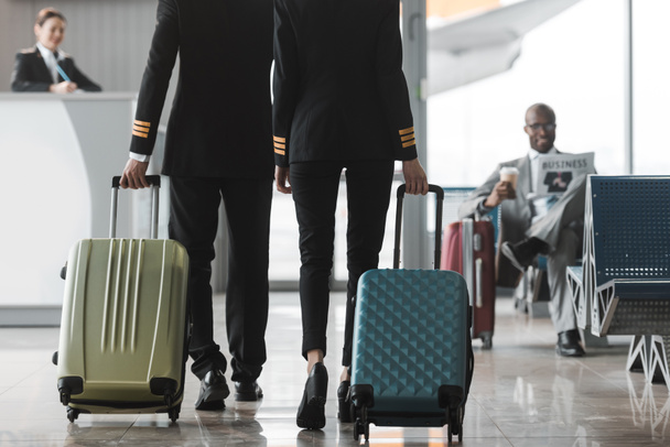 przycięte strzał pilotów płci męskiej i żeńskiej spaceru w holu lotniska z walizkami - Zdjęcie, obraz