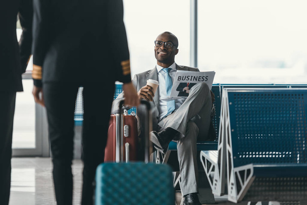 knappe jonge zakenman kijken vrouwelijke piloot passerende terwijl het wachten op de vlucht op de luchthaven lobby - Foto, afbeelding
