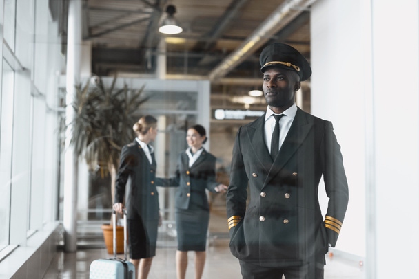 thoughtful young pilot in airport with stewardesses before flight - Photo, Image