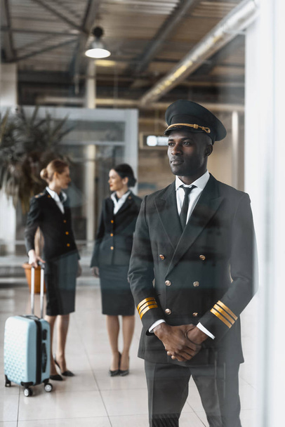 handsome young pilot in airport with stewardesses before flight - Photo, Image