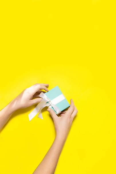Top view female hands opening turquoise gift box with white ribbon - 写真・画像
