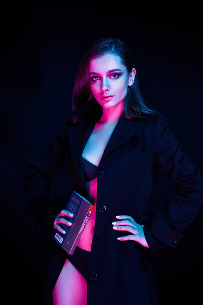Gorgeouns young fashion model in lingerie and black coat holding book - Foto, afbeelding