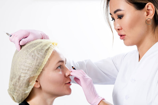 Kozmetikai eljárást, amely segítségével a Botox injekciók arccsontja korrekciója. Nő ázsiai orvos defekt botox-a járomcsontján, egy fiatal nő - Fotó, kép