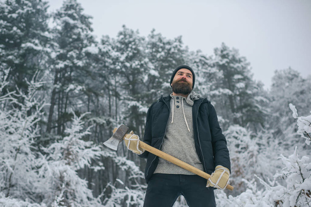 Bearded man with axe in snowy forest. - Zdjęcie, obraz