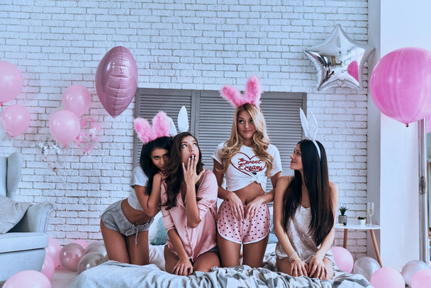 Four playful young smiling women in bunny ears sitting on bed with balloons  - Fotoğraf, Görsel