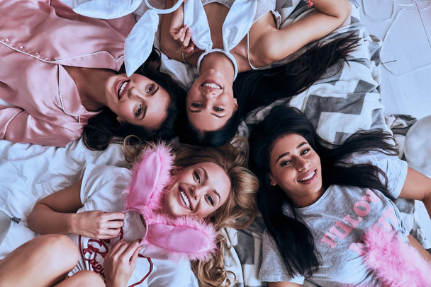 Top view of four beautiful young women in pajamas holding bunny ears  - Φωτογραφία, εικόνα