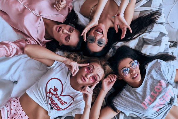 Top view of four beautiful young women smiling while lying on bed in pajamas  - Фото, зображення