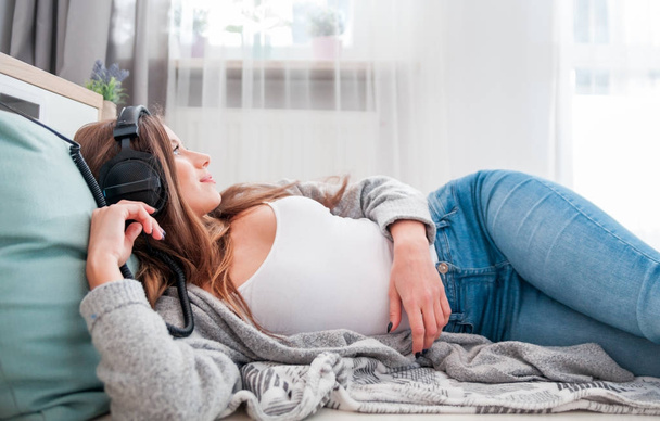 Young woman with headphones lying on floor listening to music at - Photo, Image
