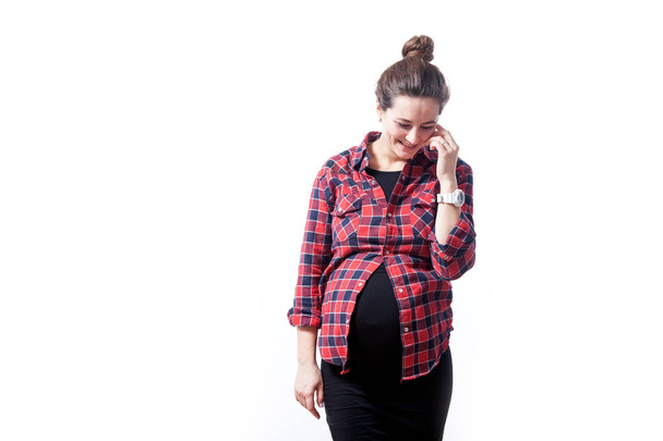 Veselá mladá tmavovlasá žena v kostkované košili a černých šatech na konci těhotenství s úsměvem a Pózování na bílém pozadí izolované - Fotografie, Obrázek