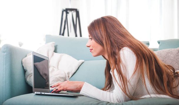 Confident woman at home lying on sofa and working with laptop - Photo, Image