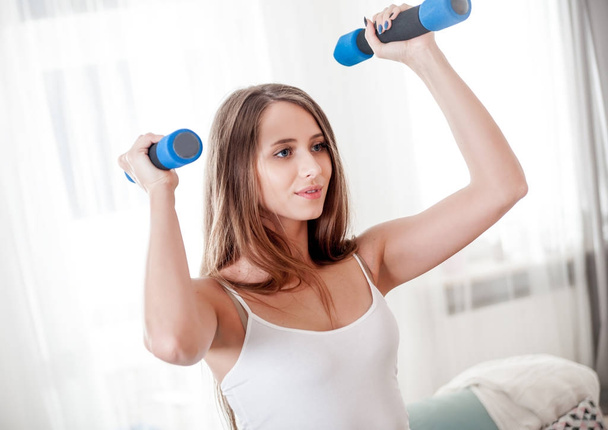 Sporty young woman exercising at home with dumbbells - Photo, image