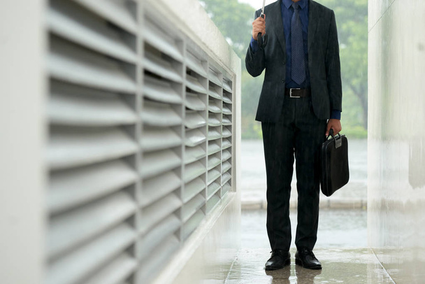 Porträt eines nicht wiederzuerkennenden Geschäftsmannes, der mit Regenschirm im Freien steht - Foto, Bild