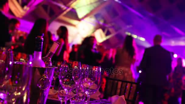 eine Jugendparty in einem Restaurant oder einer Diskothek, Banketttische mit Alkohol und Essen vor dem Hintergrund der Silhouetten tanzender Menschen, Bühnenlicht und violette Farbe - Filmmaterial, Video
