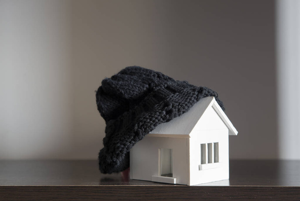 το σπίτι το χειμώνα - θέρμανσης σύστημα έννοια και κρύο χιονισμένο καιρικές συνθήκες με το μοντέλο του ένα σπίτι φορώντας ένα πλεκτό κάλυμμα - Φωτογραφία, εικόνα
