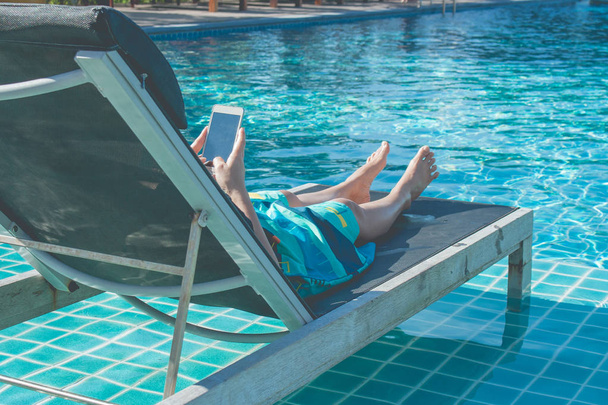 Mujer tumbada en la cama y jugando su smartphone junto a la piscina. (enfoque selectivo
) - Foto, imagen