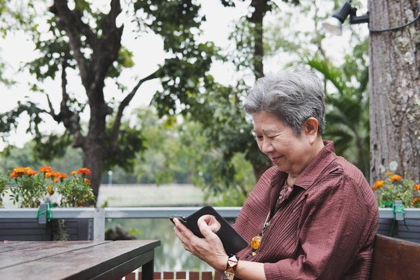 anciana sosteniendo teléfono móvil en el jardín. texti femenino de edad avanzada
 - Foto, Imagen