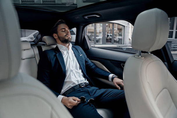 Tired young man in full suit keeping eyes closed while sitting in car, Feeling overworked - Foto, imagen