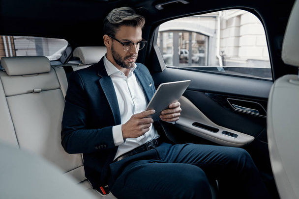 Confident young man in suit using digital tablet while sitting in car - Φωτογραφία, εικόνα