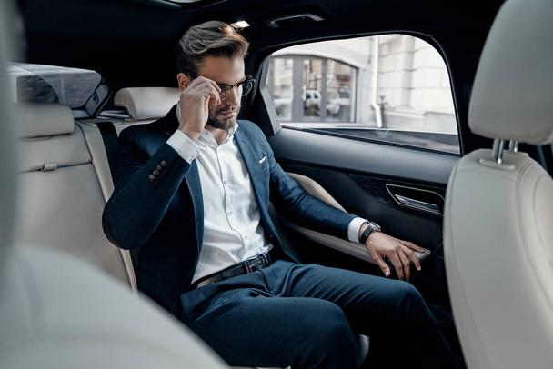 Handsome young man in  suit adjusting his eyewear while sitting in car - Fotó, kép
