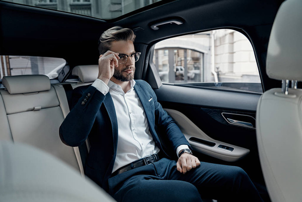 Handsome young man in suit adjusting his eyewear while sitting in car - Foto, afbeelding