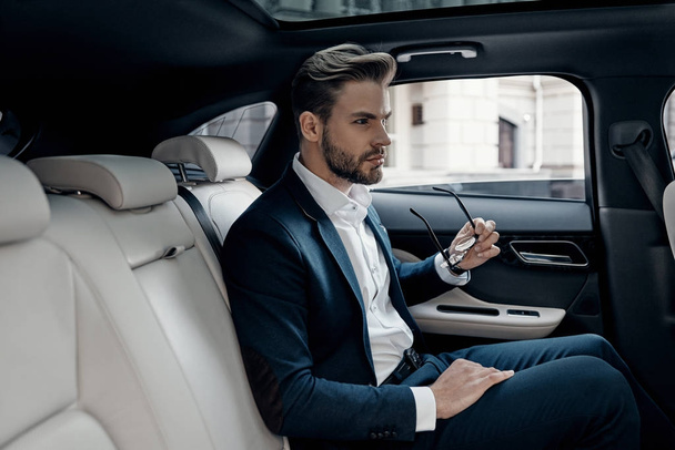 Confident businessman sitting in car and holding eye wear - Foto, imagen