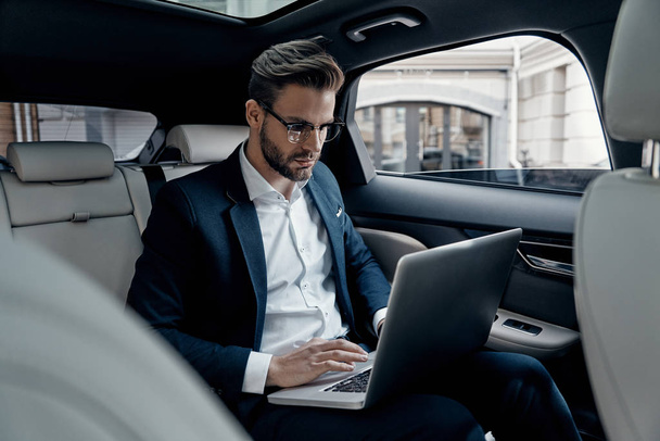 Confident young man in suit using laptop while sitting in car - Foto, Imagem
