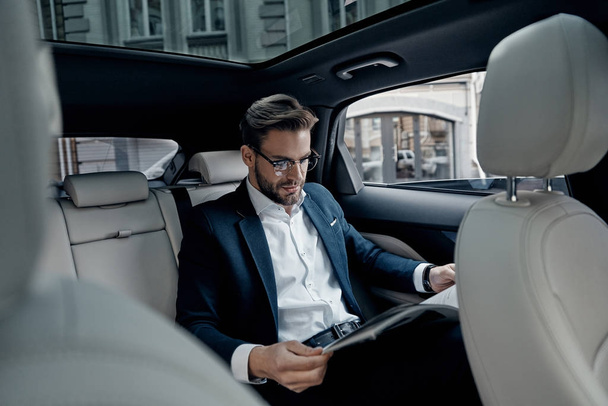 Przystojny, młody biznesmen w kolorze czytania Aktualności w gazecie, siedząc w samochodzie - Zdjęcie, obraz