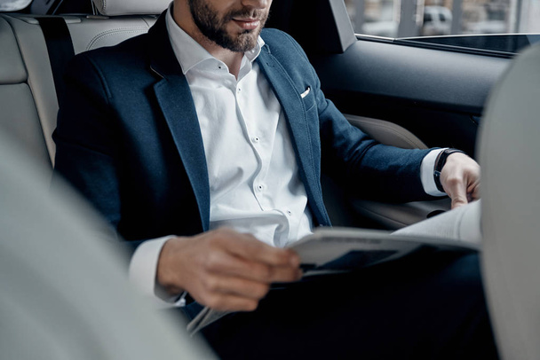 Close up of young man in suit reading a newspaper while sitting in car - Fotoğraf, Görsel