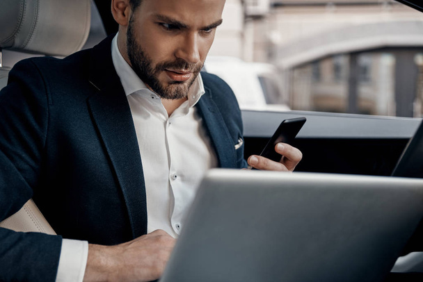 Confident young man in suit using laptop while sitting in the car - Foto, imagen