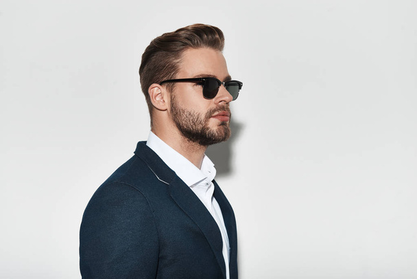 Handsome young man in formal wear and sunglasses posing in studio - Фото, зображення