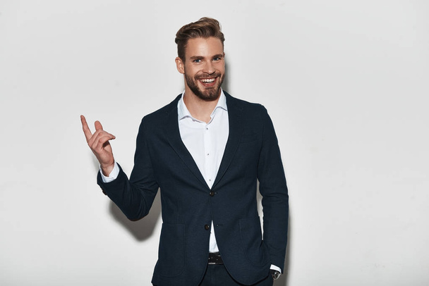 Handsome young man in formal wear pointing finger up and smiling in studio - Φωτογραφία, εικόνα