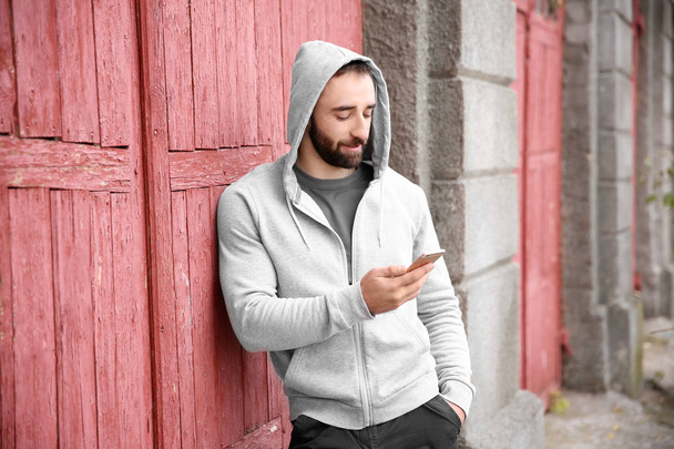 Portrait of young hipster man with phone outdoors - Fotó, kép