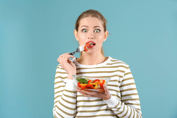 Young beautiful woman eating fresh salad on color background - Foto, afbeelding