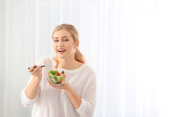 Young beautiful woman eating fresh salad on light background - Photo, image