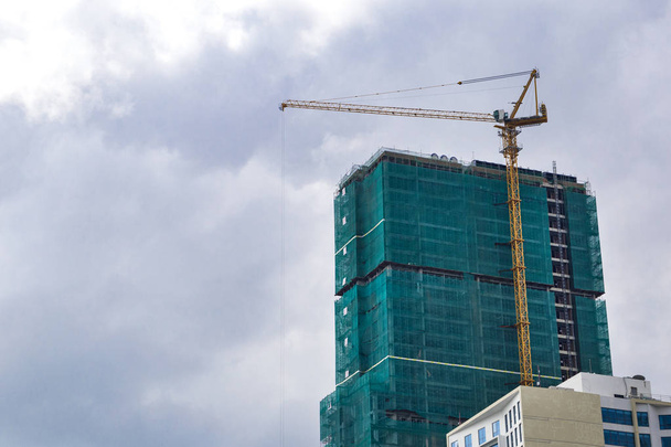 construcción de un edificio de gran altura en andamio y dos grúas de construcción amarillas en el fondo del cielo azul nublado
 - Foto, Imagen