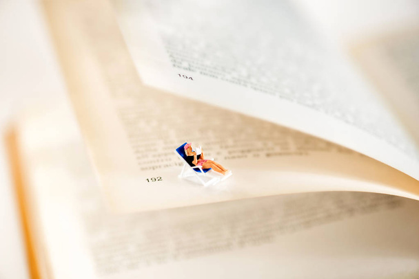 Miniature woman sitting between pages of a book - Photo, Image