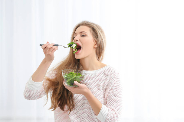 Young beautiful woman eating fresh salad on light background - Valokuva, kuva