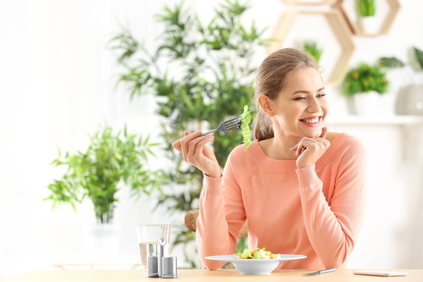 Νεαρή όμορφη γυναίκα τρώει φρέσκια σαλάτα στο σπίτι - Φωτογραφία, εικόνα