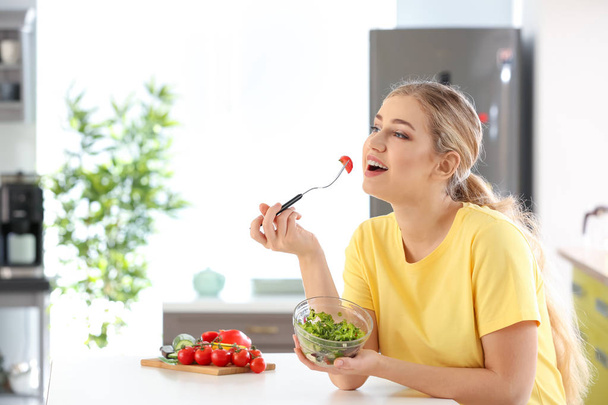 Young beautiful woman eating fresh salad in kitchen - Valokuva, kuva