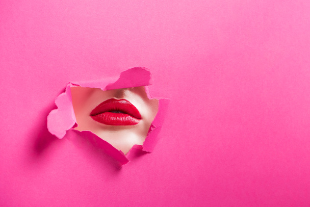 cropped image of passionate girl showing lips in hole in pink paper - Foto, afbeelding