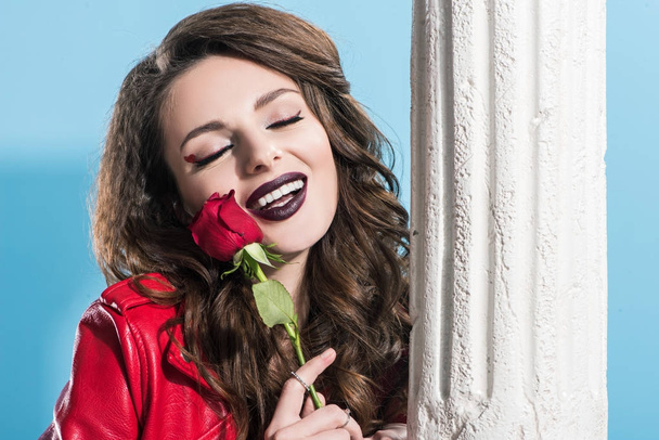 happy stylish girl with closed eyes holding red rose on blue, valentines day concept   - Photo, Image