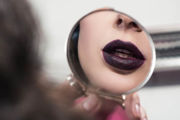 bijgesneden afbeelding van aantrekkelijk meisje met donkere lippen spiegel kijken - Foto, afbeelding