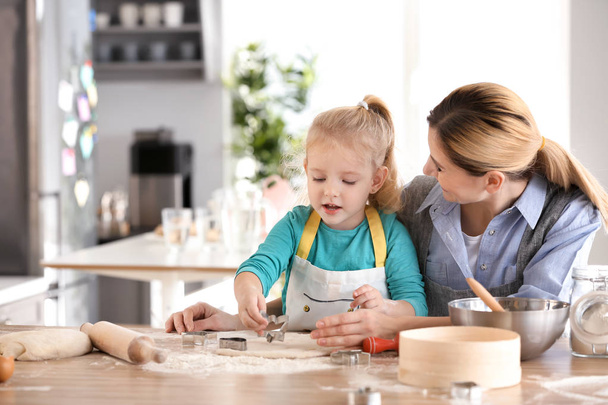 Mother and daughter with dough at table indoors - Foto, afbeelding