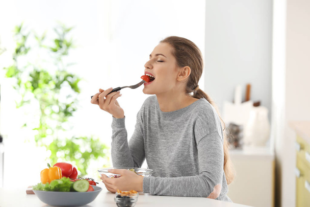 Young beautiful woman eating fresh salad in kitchen - Photo, Image