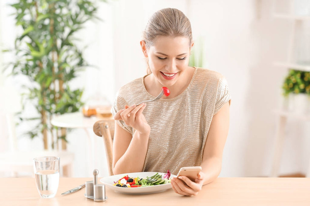 Young beautiful woman with phone eating fresh salad at home - Foto, immagini