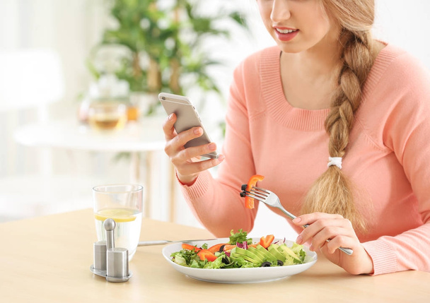 Young beautiful woman with phone eating fresh salad at table - Valokuva, kuva